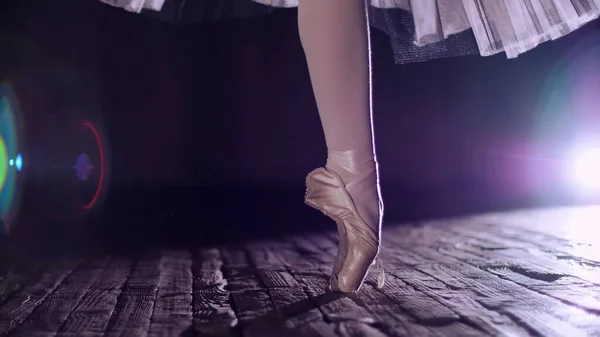 close up, in rays of spotlight, on stage of old theater hall. ballerina in white ballet skirt, rotates on toe in pointe shoe, performs elegantly a certain ballet exercise, tour,pointe. High quality