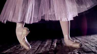 close up, in rays of spotlight, on stage of old theater hall. ballerina in white ballet skirt, raises on toes in pointe shoes, performs elegantly a certain ballet exercise, pointe ,tendu. High quality