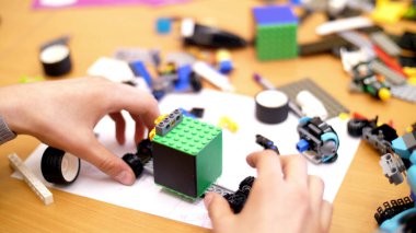 close-up, childrens hands hold a multicolored small robot, machine, assembled from a designer. children are fond of robotics, programming, modeling,. High quality photo