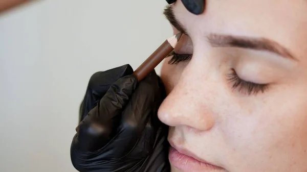 beauty saloon. Eyebrow correction. close-up, cosmetologist, browmaker, master in black gloves, draws with special pencil the shape of eyebrows before applying eyebrow dye. High quality photo