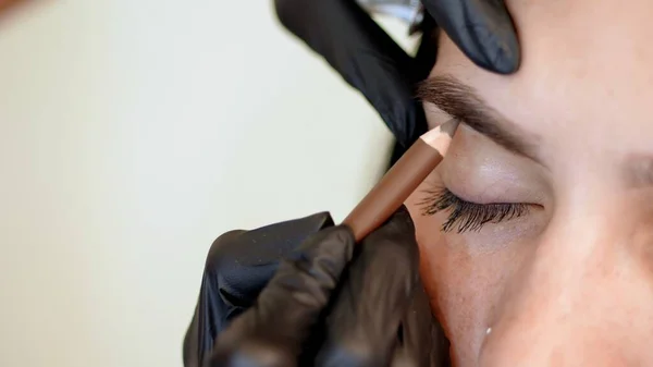 beauty saloon. Eyebrow correction. close-up, cosmetologist, browmaker, master in black gloves, draws with special pencil the shape of eyebrows before applying eyebrow dye. High quality photo