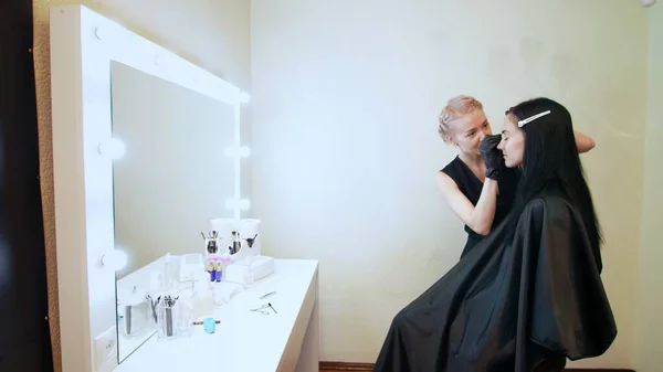 beauty saloon. the cosmetician in black rubber gloves hold tweezers and pull out eyebrows. Master corrects the shape of the eyebrows. near a large mirror with illumination. High quality photo