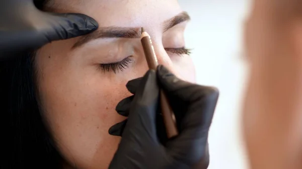 beauty saloon. Eyebrow correction. close-up, cosmetologist, browmaker, master in black gloves, draws with special pencil the shape of eyebrows before applying eyebrow dye. High quality photo