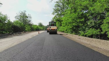 repair of a highway, roller compactor machine and asphalt finisher laying a new fresh asphalt pavement, covering on one side of the traffic. Road construction works. High quality photo