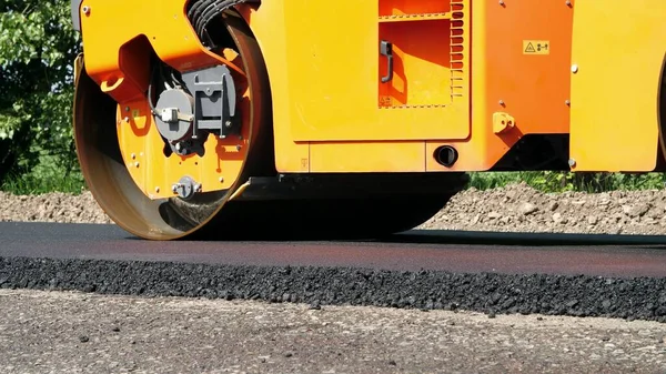 close-up, Road construction works with roller compactor machine and asphalt finisher. Road roller laying fresh asphalt pavement on top of the gravel base during road construction. High quality photo