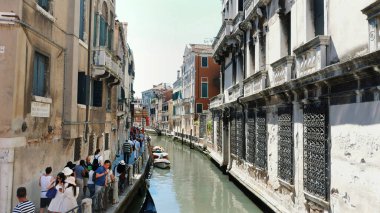 VENICE, ITALY - JULY 7, 2018: narrow canal between the ancient houses of Venzia, hot summer day. tourists walk along the ancient streets along the canals. High quality photo