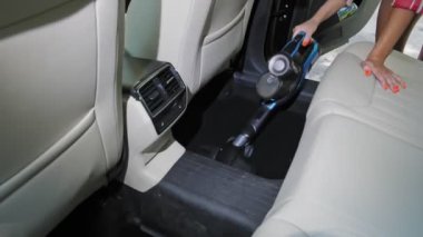 Araba temizliği. Yakın plan. Kadın elektrikli süpürge kullanarak otomobil kulübesinin içini süpürüyor.