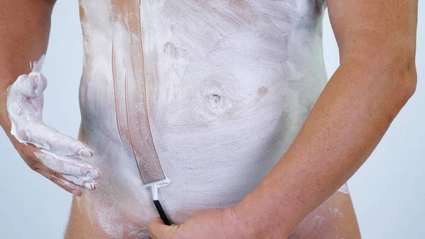Kafkasyalı çıplak adam vücudunu, gövdesini, bikini bölgesini jiletle tıraş ediyor, tıraş köpüğü sürüyor. Yüksek kalite fotoğraf