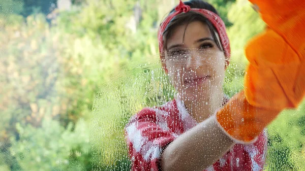 view through the window, smiling Beautiful woman in gloves, Cleaning Window by spraying Cleaning Products, using detergent and rag. worker of cleaning service or housewife. High quality photo