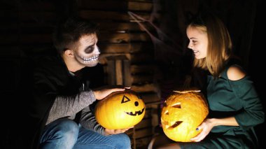 Cadılar Bayramı partisinde, gecede, alacakaranlıkta, ışık ışığında, kostümlü ve korkunç makyajlı bir kızla bir adam iki büyük Cadılar Bayramı balkabağı tutuyor. Yüksek kalite fotoğraf