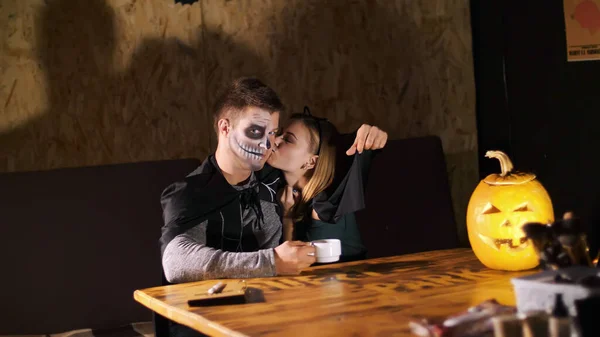 date in style of Halloween party, night, twilight, in the rays of light, guy with a girl dressed in costumes and with a terrible makeup are kissing. High quality photo