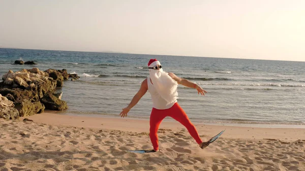 Santa Claus summer vacation. Father Christmas having fun. Funny Santa, in flippers runs through sandy beach to the sea. He is in a hurry to swim, snorkel. back view. High quality photo