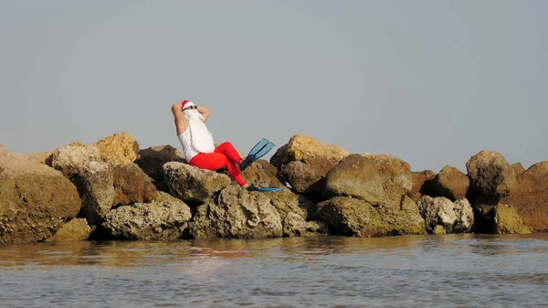 산타클로스는 일광욕을 산타클로스가 재밌게 해변의 바위에 선글라스와 오리발을 재밌는 클로스의 — 스톡 사진