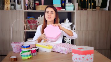 Hediyeler paketleniyor. Çekici bir kadın, hediye ve dekorasyon tasarımcısı çevrimiçi eğitim programları, video bloğunu kaydediyor, giyim kuşamını takıyor, akıllı telefonun ve kameranın önünde oturuyor. Online satış. Yüksek kalite fotoğraf