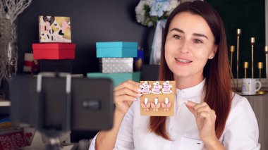 Tasarımcı hediye paketliyor. Çekici kadın dekoratör online yayın, konferans, video blogu, web sitesi, akıllı telefonun önünde duruyor. İnternette çalışıyorum. Yüksek kalite fotoğraf