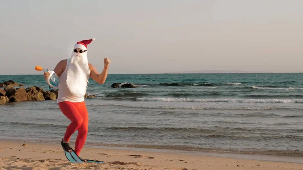 Santa Claus summer vacation. Santa Claus having fun. Funny Santa, in sunglasses and flippers, is dancing on beach by the sea and relaxing. Santa going to snorkel. High quality photo