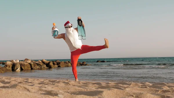 Santa Claus summer vacation. Father Christmas, having fun. Santa Claus doing yoga. Funny Santa, in sunglasses, with flippers and snorkeling mask, on beach by the sea. Santa going to snorkel. High