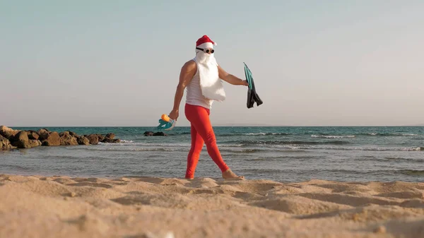 클로스의 산타클로스가 재밌게 선글라스를 오리발 스노클링 마스크를 재미있는 해변을 달리고 — 스톡 사진
