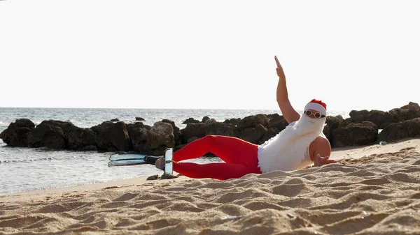 Santa Claus summer vacation. Santa Claus having fun. Funny Santa, in flippers, relaxing while lying on sandy beach by the sea. High quality photo