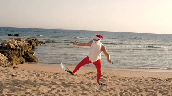 Santa Claus summer vacation. Father Christmas having fun. Funny Santa, in flippers runs through sandy beach to the sea. He is in a hurry to swim, snorkel. back view. High quality photo