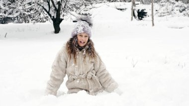 Karlı kış eğlencesi. Sıcak kış kıyafetleri giymiş mutlu, sevimli, güzel kız, kar yağarken, kar altında, dışarıda, kar yağışlı kış gününde, parkta ya da ormanda kar atıyor. Yüksek kalite