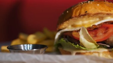 Hamburger. Yemek pişirmek. fast food. Yakın plan. Patates kızartmalı burger. Etli, sebzeli ve sahanda yumurtalı sulu burger. Patates kızartması ve domates sosuyla servis edilen hamburger. döndür.
