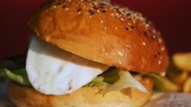 Hamburger. Yemek pişirmek. fast food. Yakın plan. Patates kızartmalı burger. Etli, sebzeli ve sahanda yumurtalı sulu burger. Patates kızartması ve domates sosuyla servis edilen hamburger. döndür.