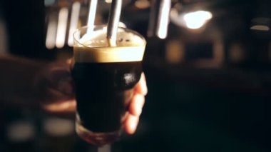 Barmen bardağa bira doldurur. Barmenlerin ellerinin bardakları koyu birayla doldurduğu yakın çekim. Bar masasında, barda. Bira barında bardağa bira dolduruyorum.