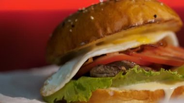 Hamburger. fast food. Yakın plan. Etli, sebzeli ve sahanda yumurtalı sulu burger. Döndürme. yemek yapmak
