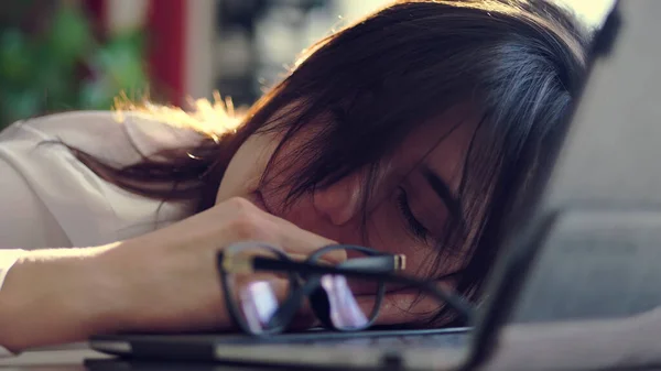 疲れの若いビジネスマンの女性は 彼女のオフィスの仕事で机の上にノートパソコンの上で寝て 眼鏡を削除します 仕事に圧倒されポートレートショット 高品質の写真 ストック写真
