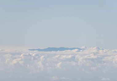 Mavi gökyüzü ve arkasında dağın zirvesi olan beyaz bulutlar.