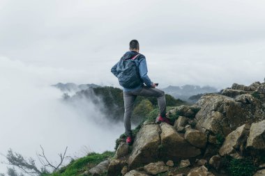 Teçhizatlı yalnız bir adam dağın tepesinde birden fazla sis var.