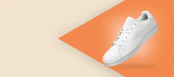 Banner with new pair of white sneakers isolated on light yellow and orange background. Sportive pair of shoes for mockup. Fashionable stylish sports casual shoes.