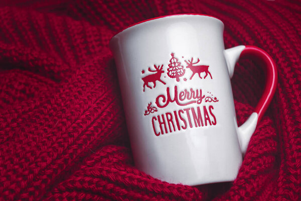 Still life of Christmas concept with Merry Christmas mug on warm and red sweater. Merry Christmas mug on cozy red sweater. Christmas and winter concept.