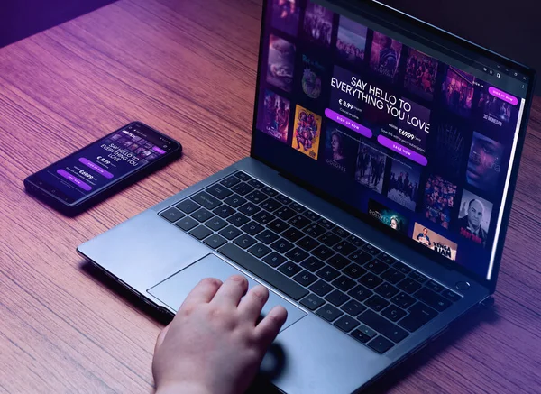 Genç bir kadın dizüstü bilgisayardan HBO Max izliyor. Dizüstü bilgisayarda HBO Max logosu ve akıllı telefon ekranları. Dizüstü bilgisayarlı ahşap masa ve akıllı telefon HBO maksimum.