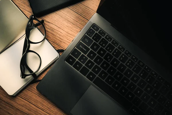 Top view of wood vintage desk focused on laptop with notepad, smartphone and glasses. Workplace. Work from home. Office desk.