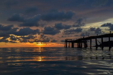 Tayland, Koh Kood Adası. Gün batımlı güzel bir atmosfer. Sıcak deniz, ahşap iskele, tatlı ve acı verici mutluluk hissi. Güzel günbatımı renkleri, batan güneşin aydınlattığı bulutlar. Denizde gün batımının yansıması.