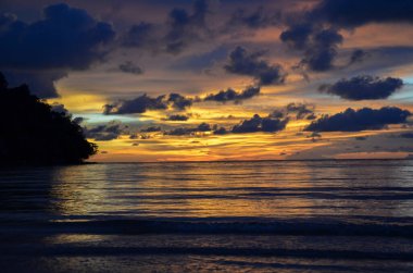 Tayland, Koh Kood Adası. Gün batımlı güzel bir atmosfer. Sıcak deniz, ahşap iskele, tatlı ve acı verici mutluluk hissi. Güzel günbatımı renkleri, batan güneşin aydınlattığı bulutlar. Denizde gün batımının yansıması.
