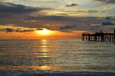 Tayland, Koh Kood Adası. Gün batımlı güzel bir atmosfer. Sıcak deniz, ahşap iskele, tatlı ve acı verici mutluluk hissi. Güzel günbatımı renkleri, batan güneşin aydınlattığı bulutlar. Denizde gün batımının yansıması.