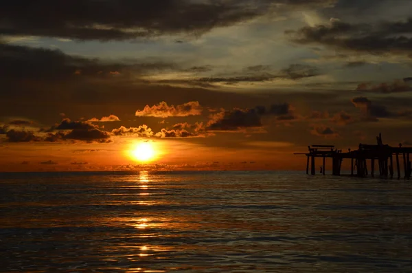 Tayland, Koh Kood Adası. Gün batımlı güzel bir atmosfer. Sıcak deniz, ahşap iskele, tatlı ve acı verici mutluluk hissi. Güzel günbatımı renkleri, batan güneşin aydınlattığı bulutlar. Denizde gün batımının yansıması.