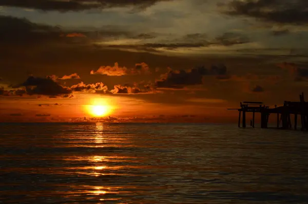 Tayland, Koh Kood Adası. Gün batımlı güzel bir atmosfer. Sıcak deniz, ahşap iskele, tatlı ve acı verici mutluluk hissi. Güzel günbatımı renkleri, batan güneşin aydınlattığı bulutlar. Denizde gün batımının yansıması.