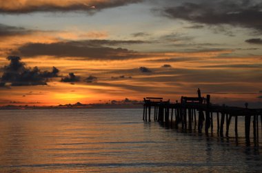 Tayland, Koh Kood Adası. Gün batımlı güzel bir atmosfer. Sıcak deniz, ahşap iskele, tatlı ve acı verici mutluluk hissi. Güzel günbatımı renkleri, batan güneşin aydınlattığı bulutlar. Denizde gün batımının yansıması.