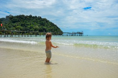Tayland, Koh Kood Adası. Beyaz kumu, hindistan cevizi palmiyeleri ve gök mavisi denizi olan güzel bir plajda bir çocuk. Plajda salıncak olan romantik bir yer. Sıcak deniz, gün batımı. Kısacası, dünyadaki cennet. Mükemmel bir tatil. Sahilde ahşap bir iskele..
