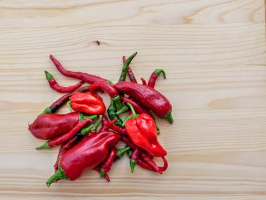 Arkaplan, ahşap bir tahtaya yerleştirilmiş farklı kırmızı biberlerden oluşuyor. Kuş, habanero ve espelette biberi..