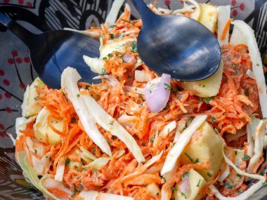 Beyaz lahana, havuç, elma, balzamik sirke ve baldan yapılmış ev yapımı lahana salatası. Gri bir toprak kabında servis edilmiş.. 