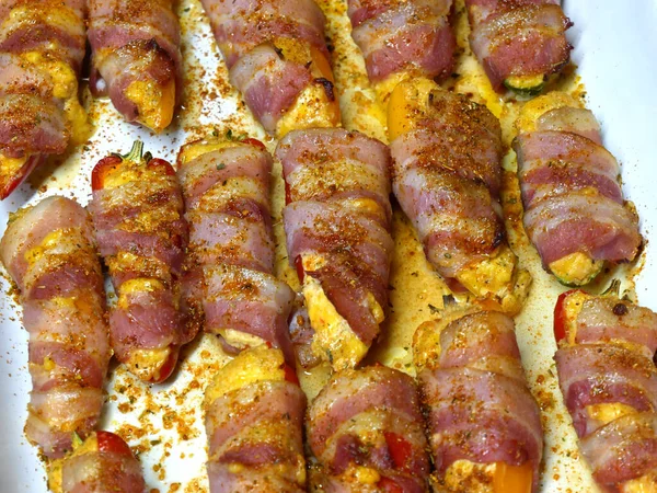 Preparation of a dish called Jalapeno poppers, composed of jalapeno peppers stuffed with cheese, sopasco and rolled with a slice of smoked bacon.