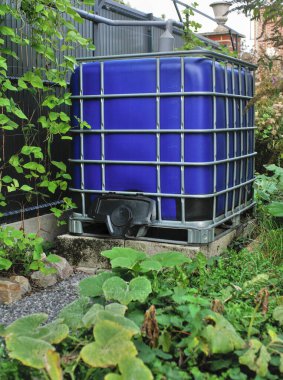 Rainwater collection tank, with blue walls, in a green setting. clipart