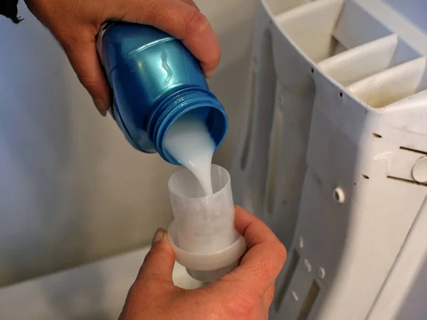 fabric softener is poured into a measuring cup near a washing machine.