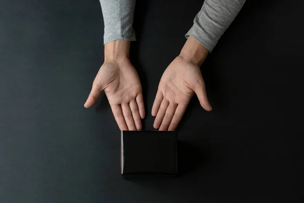 Man hands giving a black box over a black background