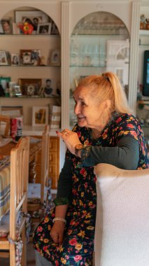 Yetmiş yaşındaki sarışın kadın etrafa saldırıyor, yan tarafa bakıyor ve elleriyle, dikey görüntüsüyle, doğal güneş ışığıyla gebe kalıyor.